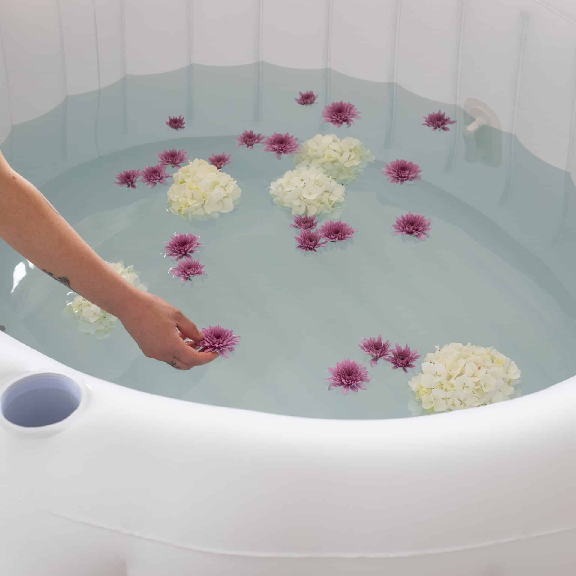 Bloom Birth Pool - filled with water and flowers with a hand placing a single flower in pool